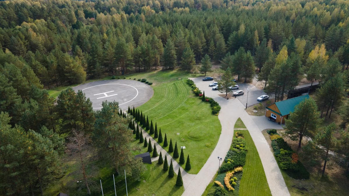 Aerial shot of a forest with a helipad, parking area, and landscaped gardens.
